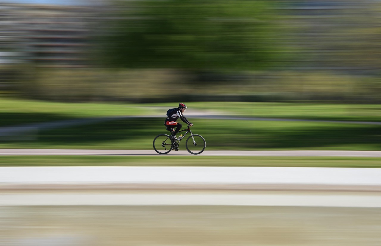 A cyclist rides across a green landscape while strong horizontal motion blur streaks the background.